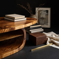 Corner detail of oval coffee table on a drum base with an open shelf beside wood, brass and linen samples