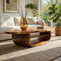Oval coffee table on a drum base with an open shelf in a sunlit room with large windows and plants