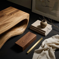 Corner detail of curved side coffee table with a wave tunnel beside wood, brass and linen samples