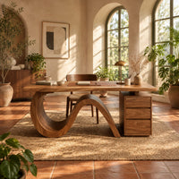Desk with a looping wave base and a drawer pedestal in a bright home office with arched windows and plants