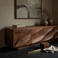 Corner detail of TV cabinet with four faceted sculpted doors beside wood, brass and linen samples