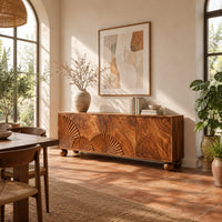 Wooden sideboard with fan carved relief on four door fronts and ball feet in a bright dining room with arched windows and plants