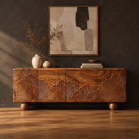 Sideboard carved with fan shaped leaves on four doors and ball feet in a dark studio against a charcoal plaster wall