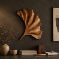 Detail of fan shaped carved leaf wall art with radiating ribs and a curved stem beside wood, brass and linen samples