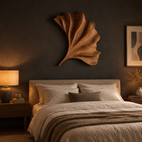 Fan shaped carved leaf wall art with radiating ribs and a curved stem above a bed in a dusk lit bedroom