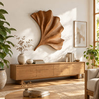 Fan shaped carved leaf wall art with radiating ribs and a curved stem in a bright sunroom with green plants