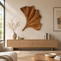 Fan shaped carved leaf wall art with radiating ribs and a curved stem above a light oak sideboard in daylight