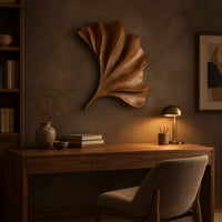Fan shaped carved leaf wall art with radiating ribs and a curved stem above a desk in a dark study corner