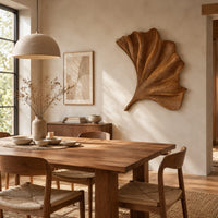 Fan shaped carved leaf wall art with radiating ribs and a curved stem beside a dining table in natural light