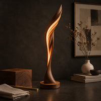 Corner detail of tall twisting floor lamp shaped like a leaf with a glowing seam beside wood, brass and linen samples