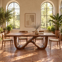 Rectangular dining table on an infinity loop base of curved wood in a bright dining room with arched windows and plants