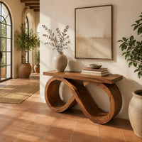 Console table with an infinity loop base and a plank top in a bright entryway with arched windows and plants