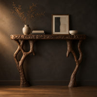 Fireplace mantel with a carved top slab and twisted branch shaped legs in a dark studio against a charcoal plaster wall