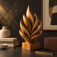 Corner detail of flame shaped sculpture of layered carved leaves on a square wooden base beside wood, brass and linen samples