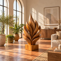 Flame shaped sculpture of layered carved leaves on a square wooden base in a bright living room with arched windows and plants