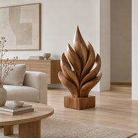 Flame shaped sculpture of layered carved leaves on a square wooden base in a Scandinavian living room with white walls