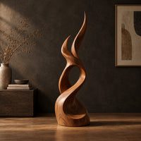 Flame shaped wood sculpture with two pointed tips and a swirling base in a dark studio against a charcoal plaster wall