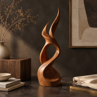 Corner detail of flame shaped wood sculpture with two pointed tips and a swirling base beside wood, brass and linen samples