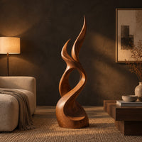 Flame shaped wood sculpture with two pointed tips and a swirling base in a dark living room at golden hour