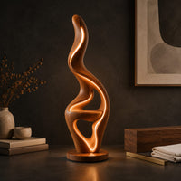 Corner detail of flame shaped floor lamp with a glowing edge and a small shelf beside wood, brass and linen samples