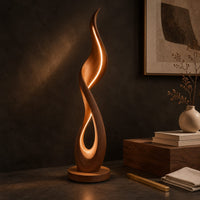 Corner detail of flame shaped floor lamp with a glowing teardrop opening on a disc base beside wood, brass and linen samples