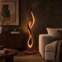 Flame shaped floor lamp with a glowing teardrop opening on a disc base in a dark living room at golden hour