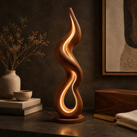 Corner detail of flame shaped wooden floor lamp with a glowing loop on a disc base beside wood, brass and linen samples