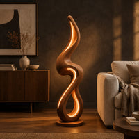 Flame shaped floor lamp with a looping wooden ribbon and glowing inner edge in a dark living room at golden hour