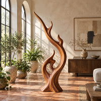 Flame shaped wood sculpture with a long sweeping arm and an open loop in a bright living room with arched windows and plants