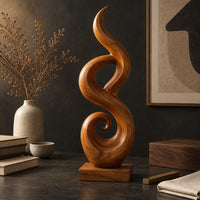 Corner detail of flowing flame sculpture with a spiral scroll at its foot and a block base beside wood, brass and linen samples