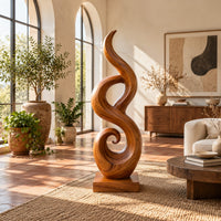 Flowing flame sculpture with a spiral scroll at its foot and a block base in a bright living room with arched windows and plants