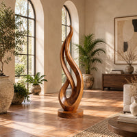 Flame shaped wood sculpture with an open loop on a disc base in a bright living room with arched windows and plants
