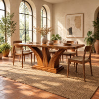 Rectangular dining table with two flared pedestal legs on a stepped plinth in a bright dining room with arched windows and plants