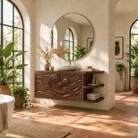 Floating cabinet with carved swirling wave front and open side shelves in a bright bathroom with arched windows and plants