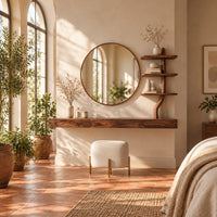 Floating wood makeup vanity with a circular mirror and a branch shaped tiered shelf in a bright bedroom with arched windows and plants
