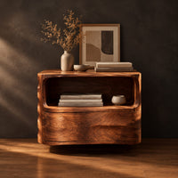 Floating nightstand with a curved open shelf and wavy carved sides in a dark studio against a charcoal plaster wall