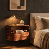 Floating nightstand with a curved open shelf and wavy carved sides in a dark bedroom at golden hour
