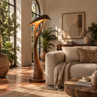 Floor lamp with a bowed stem and a hooded leaf shade in a bright living room with arched windows and plants