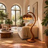 Floor lamp with an arching stem and a petal shaped shade in a bright living room with arched windows and plants