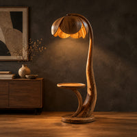 Wooden floor lamp with a flower shaped petal shade, arched stem and side tray in a dark studio against a charcoal plaster wall