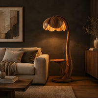 Wooden floor lamp with a flower shaped petal shade, arched stem and side tray in a dark living room at golden hour