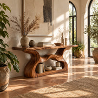 Console table with a slab top and a flowing open pedestal base in a bright entryway with arched windows and plants