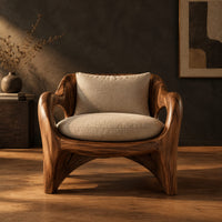 Wooden chair with sweeping open arms and cream seat and back cushions in a dark studio against a charcoal plaster wall