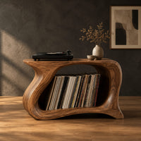 Record player stand with a flowing wave shaped body and one wide open bay in a dark studio against a charcoal plaster wall