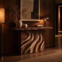 Console table with deep flowing swirl carving and a slab top in an evening entryway with walnut wall paneling