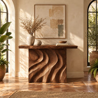 Console table with deep flowing swirl carving and a slab top in a bright entryway with arched windows and plants