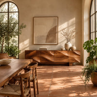 Sideboard with four flowing swirl carved panels on two block feet in a bright dining room with arched windows and plants