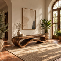 Long bench with a flat slab seat on a flowing wave base in a bright entryway with arched windows and plants