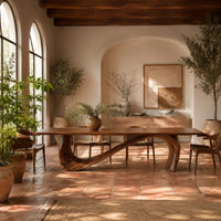 Dining table with a long smooth top on one flowing wave shaped base in a bright dining room with arched windows and plants