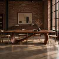 Dining table with a long smooth top on one flowing wave shaped base in an industrial loft dining room with exposed brick